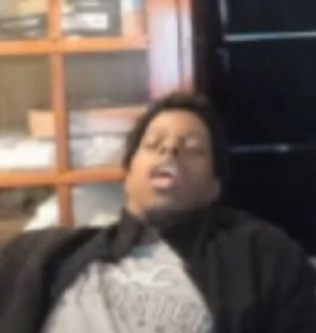 A blurry image shows a person with dark hair wearing a black and white shirt, appearing to be indoors with shelves visible in the background.