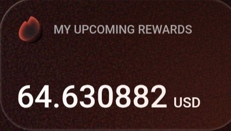 A dark red digital display showing 'MY UPCOMING REWARDS' with a balance of '64.630882 USD' next to a small flame icon.