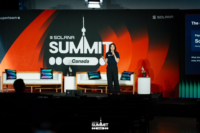 A woman speaks on stage at the Solana Summit Canada event, holding a microphone with the Solana logo and event branding displayed on a large red backdrop.