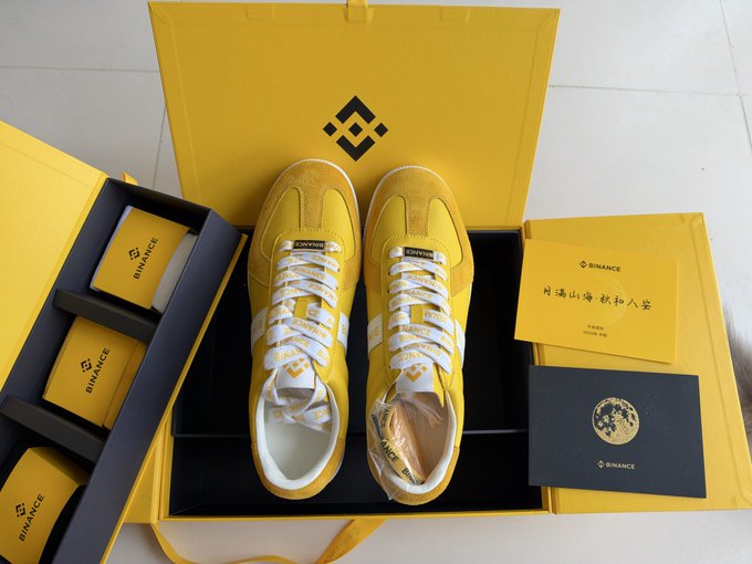 A pair of bright yellow Binance-branded sneakers is displayed in a matching yellow presentation box, accompanied by Binance-branded cards and envelopes featuring the Binance logo. The caption celebrates Mid-Autumn Festival, tying the branded merchandise to Binance's crypto wallet promotion.