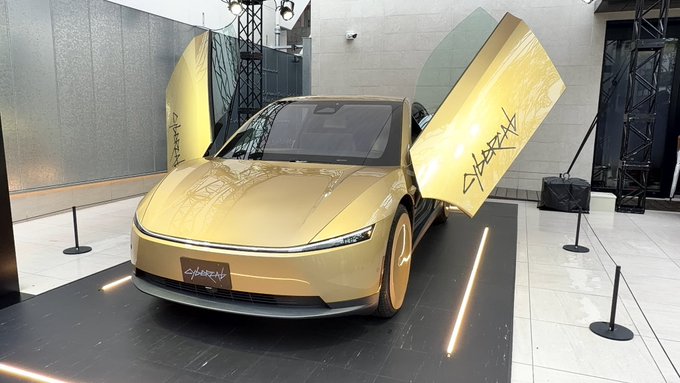 A futuristic gold-colored concept car with its gull-wing doors open on display, branded with 'CYBERSTAR' graphics.