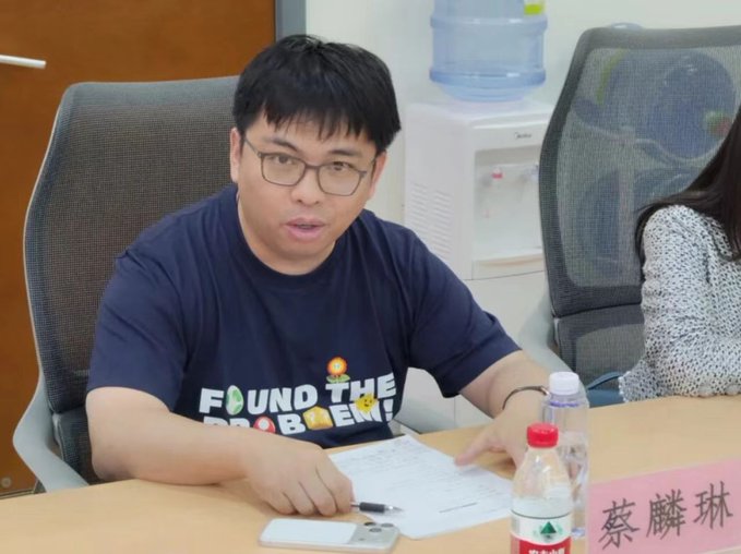 The image shows a man sitting at a table, looking down at some papers or documents while wearing glasses. There are two water bottles placed next to him on the table. The background of the image features a chair and another person who appears to be a woman with her back turned towards the camera. The post in the image is titled "Found the problem!" and has Chinese characters, which suggests that it might be related to some sort of business or project involving problem-solving or decision-making.