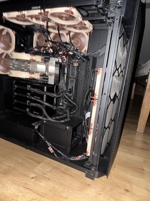 The interior of a Corsair computer case is shown with multiple pink/coral-colored fans installed at the top and front, along with bundled cables and what appears to be a power supply unit at the bottom.