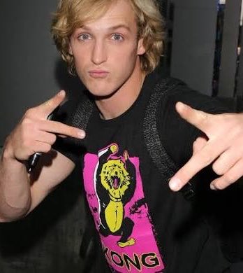 Logan Paul poses with both hands making hand gestures, wearing a black t-shirt with a pink and yellow graphic design and a backpack.