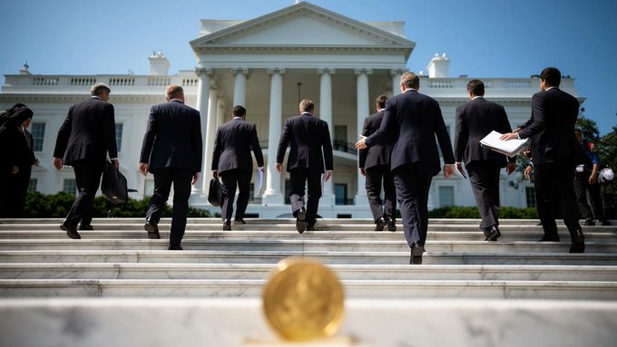 A group of men in suits walk up the steps toward the White House, with a golden object blurred in the foreground.