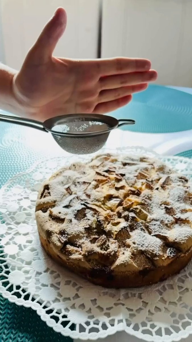 The image features an apple pie sitting on top of a lace doily on a dining table, with a person's hand holding a strainer over the pie. The background appears to be blurred, but there are some blue and white elements present as well. The caption reads "Some things are better when every step is transparent. Just like baking this apple pie: first the ingredients, then the process, a touch of powdered sugar, and finally a place at the dinner table." This message emphasizes the importance of transparency in various aspects of life, including cooking and baking.