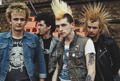 A punk rock band with spiked hair, leather vests, and edgy attire poses together against a graffiti-covered brick wall, channeling rebellious energy. The image's punk aesthetic—rooted in anti-establishment ideology—parallels the post's call to rethink conventional views on LINK's "last mile" potential, suggesting that breaking from the mainstream mindset is key to recognizing its opportunity.