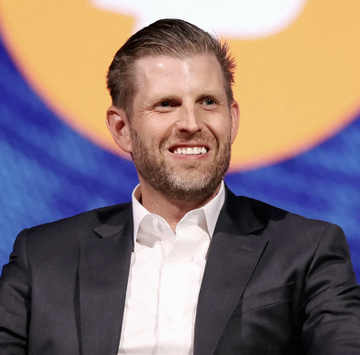 Eric Trump smiles while wearing a dark suit jacket over a white collared shirt, appearing at what looks like a panel or speaking event. The image relates to the post as it shows Eric Trump, the founder associated with American Bitcoin ($ABTC), which just expanded its corporate Bitcoin treasury with an additional 500 BTC purchase.