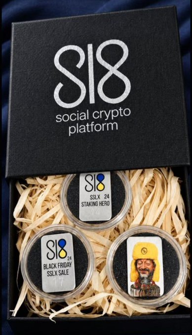 A black gift box branded with the "S18 social crypto platform" logo contains three silver coins nestled in wood shavings, labeled "SSLX '24 STAKING HERO," "BLACK FRIDAY SSLX SALE," and a third featuring a bearded man in traditional Cossack attire, promoting Sl8's staking campaign with tiered APY rewards and tokenized Ukrainian National Bank commemorative coins.