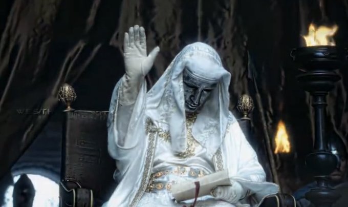 A character with pale white skin and white robes sits on a throne in a dark cavern, raising one hand while holding a book, with torches burning nearby. A watermark 'WESTU' is visible.