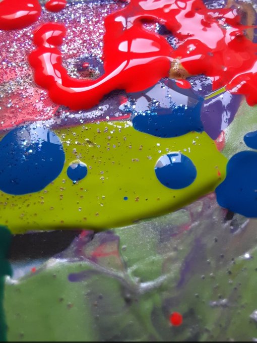 An abstract close-up shows glossy red and lime green paint blobs mixed with blue and purple on a textured surface with bubbles.