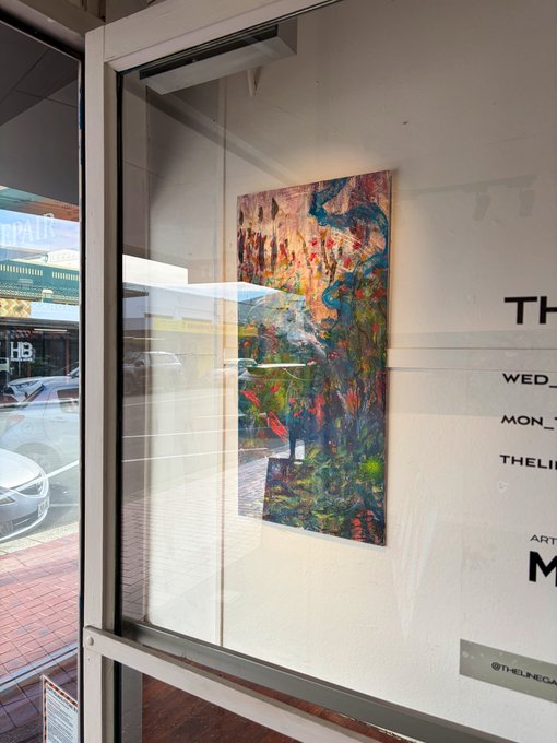 An abstract painting with vibrant colors hangs in a gallery window, with text on the glass showing days and the handle @THELINEGA.