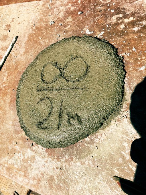 A freshly poured circular pad of wet green concrete with the words 'Old School' written into its surface, lying on a weathered wooden board.