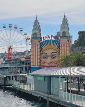 The entrance to Luna Park amusement park with its iconic face façade and towers, alongside a Ferris wheel, located near a waterfront pier.