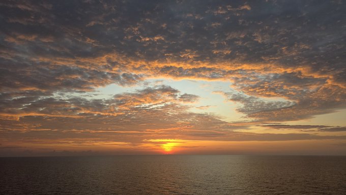 A sunset over the ocean with orange and golden clouds scattered across the sky above the horizon.