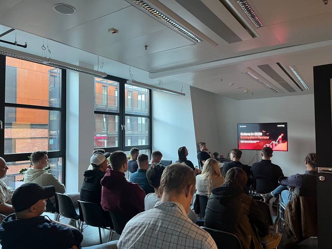 A packed room at the "Solana in 2025 Ecosystem Review" event in Gdańsk, where attendees gather for a presentation as part of a NextGen Founders event featuring speakers from Rust Poland and Optivix.