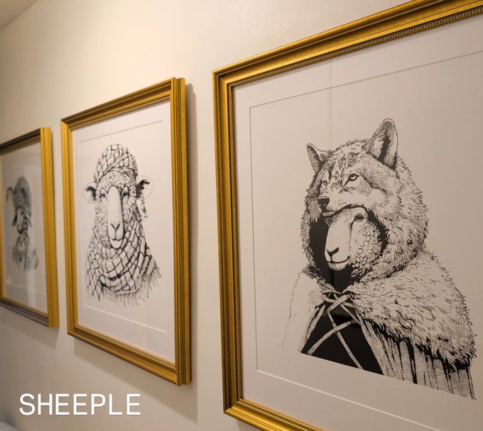 Three gold-framed black and white artworks by 'SHEEPLE' displayed on a white wall, depicting sheep-like and wolf-like figures.