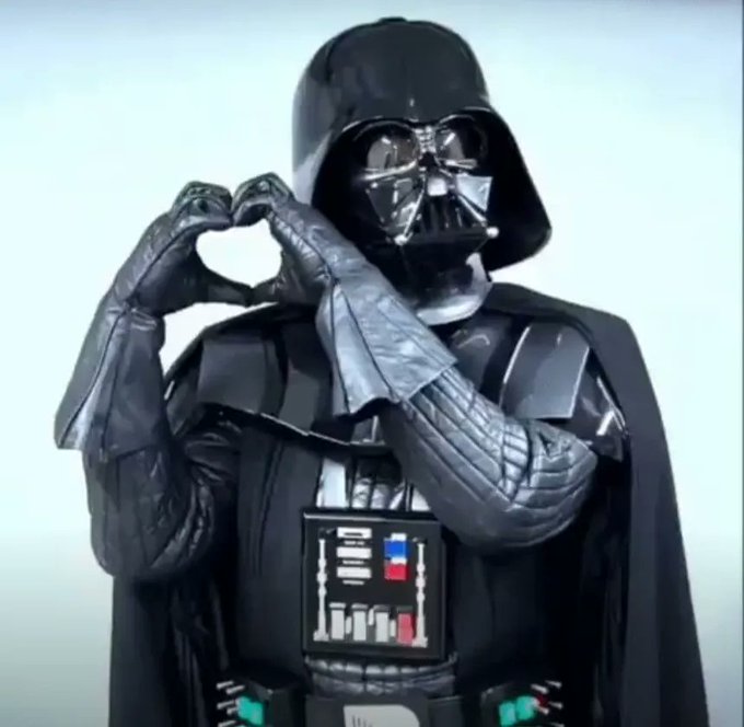 Darth Vader making a heart shape with his gloved hands against a plain white background.