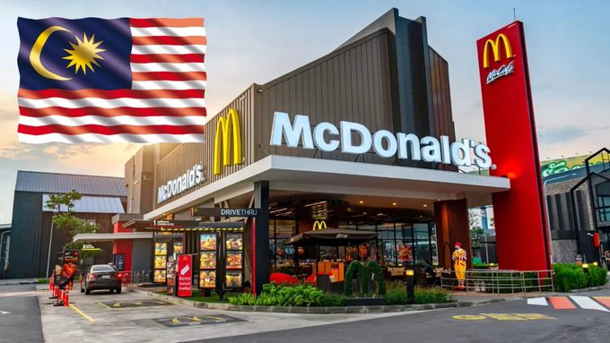 A McDonald's restaurant with its iconic golden arches and red branding, featuring a Malaysian flag overlay in the top left corner.