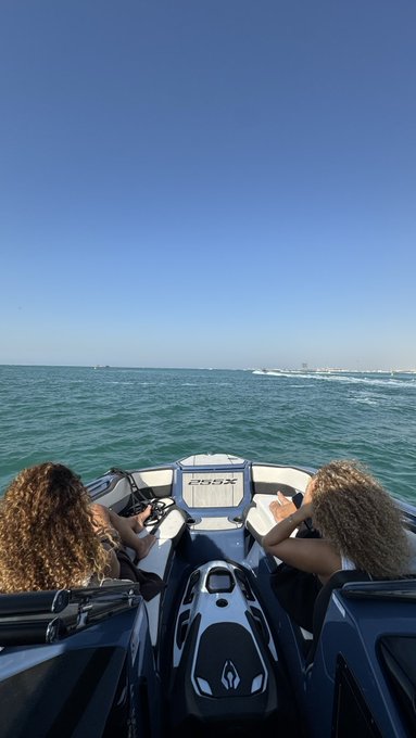 A view from behind two people riding a jet ski on the ocean under a clear blue sky.