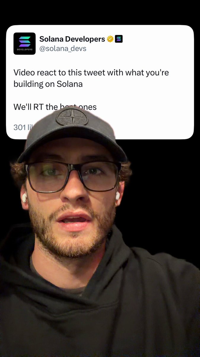The image features a man wearing glasses, a black hoodie, and a baseball cap who appears to be making a funny face or expressing surprise. The caption of the image reads "Video react to this tweet with what you're building on Solana". This suggests that the man is reacting to a post made by someone named @solanaDeveloper on Twitter about a new primitive for sport prediction, which has been developed specifically for the FIFA World Cup in the year 2006.