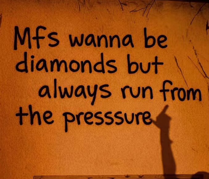 A photo of a wall sign with black text reading 'Mfs wanna be diamonds but always run from the pressure', with a hand shadow visible at the bottom.