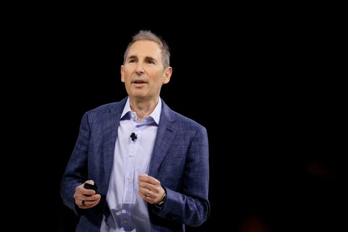 A man in a blue blazer and light blue shirt stands against a black background, gesturing while speaking at what appears to be a presentation or conference, likely Bitwise CIO Matt Hougan discussing the potential positive impact of President Trump's upcoming meeting with crypto industry executives on Bitcoin and DeFi.