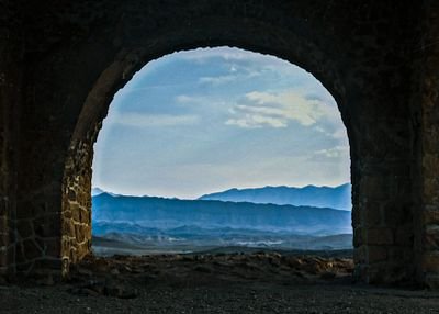 A landscape view framed by a stone archway, looking out over mountains and clouds at dusk or dawn.