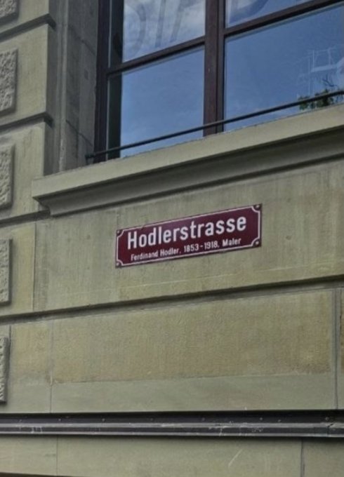 A street sign reading 'Hodlerstrasse, Ferdinand Hodler, 1853-1918, Maler' mounted on a stone building, likely a reference to the Hodler token.