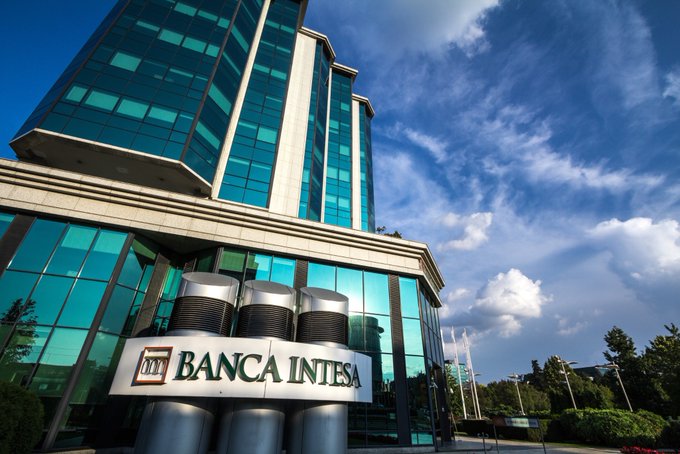 The image shows Banca Intesa's modern glass headquarters building against a blue sky, representing the Italian banking giant Intesa Sanpaolo, which has reportedly disclosed $235 million in XRP and digital asset purchases as traditional finance increasingly embraces digital assets.
