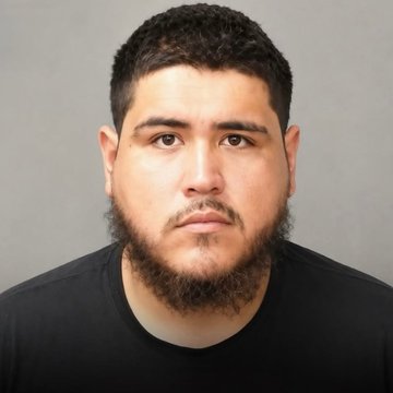 A mugshot-style photo of a man with short dark hair and a full beard, wearing a black shirt against a gray background.