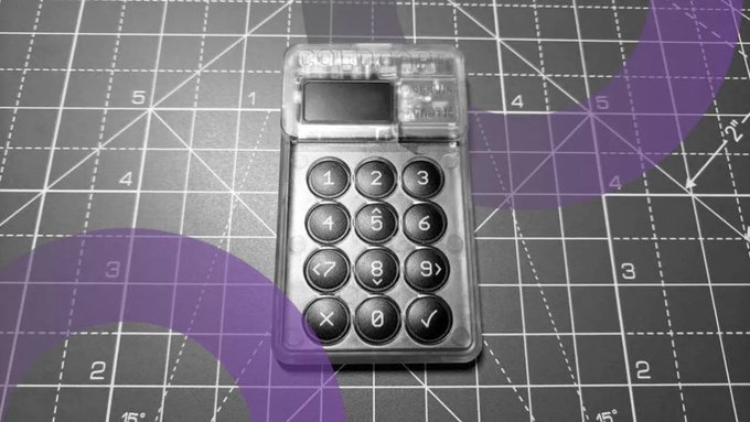 A transparent, credit-card-sized Trezor Model T cryptocurrency hardware wallet resting on a black cutting mat with purple and white measurement markings.