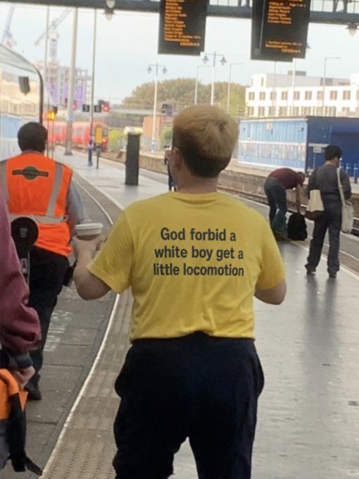A person at a train station wearing a yellow t-shirt that reads 'God forbid a white boy get a little locomotion'.