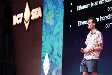 A young man in a floral-print shirt and shorts stands on stage delivering a presentation at the 'NEXT SEA' conference, with a screen behind him displaying text about Ethereum.