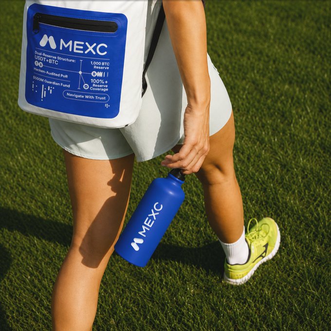 A person in athletic wear holds a blue MEXC water bottle while carrying a matching white MEXC cooler bag displaying details like "1,000 BTC Reserve," "100%+ Reserve Coverage," and "$500M Guardian Fund," embodying the post's "Touch grass. Stay hydrated. Carry MEXC wherever you go" message by blending active, outdoor living with crypto branding.