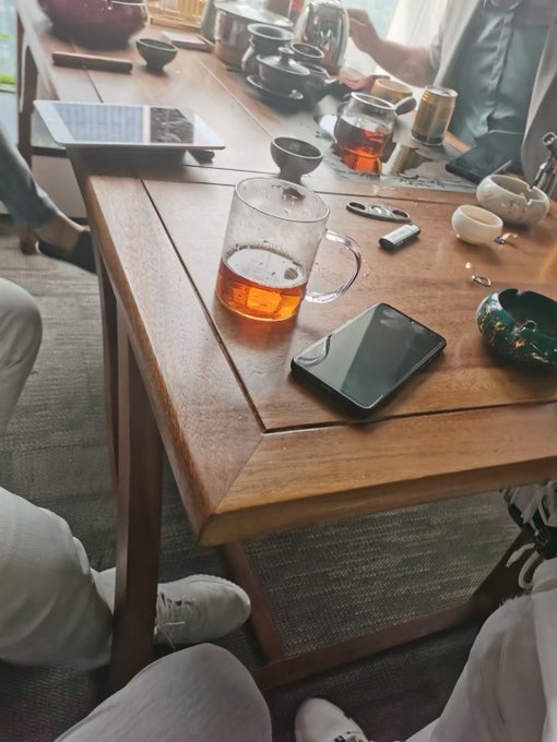 A wooden table scattered with smartphones, a glass of tea, a beer mug, and tea cups sets the scene of a casual gathering where friends discussed wealth-building in the crypto industry.
