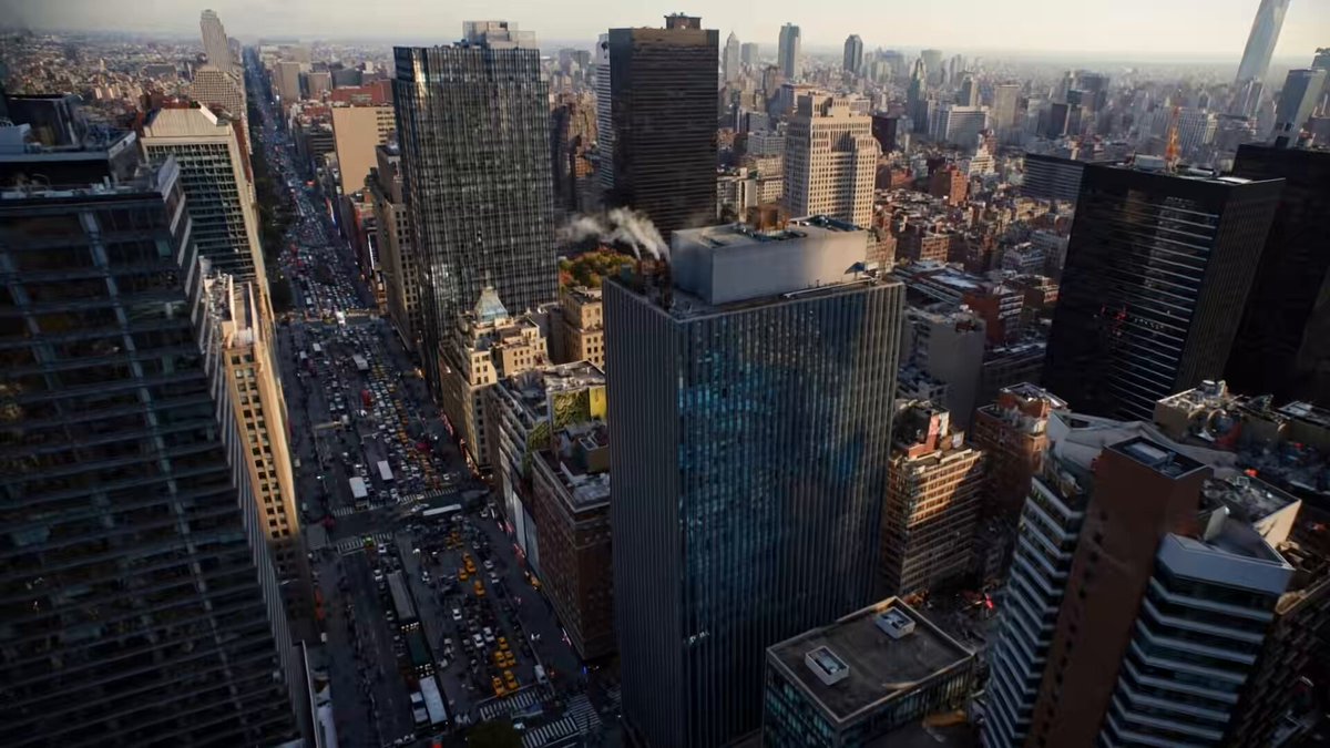 The image shows a city skyline with tall buildings, including skyscrapers and office buildings, as well as some cars driving down a busy street below. The scene appears to be taken from an aerial perspective, providing a comprehensive view of the urban landscape. The caption provided seems unrelated to the image itself and focuses on a different topic.