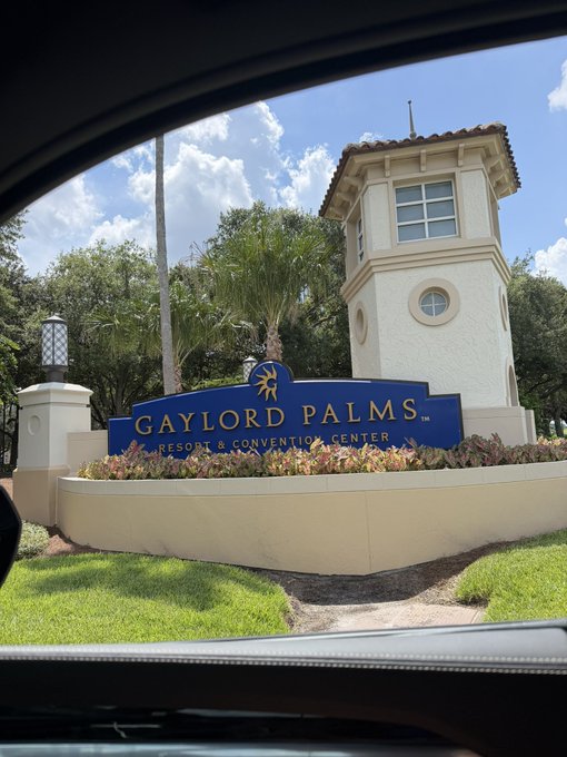 The image shows a welcoming view of the Gaylord Palms Resort & Convention Center, featuring the property's distinctive tower and signage. The image appears to be taken from inside a car, capturing the entrance as the photographer arrives at the venue where the XRP conference is taking place.