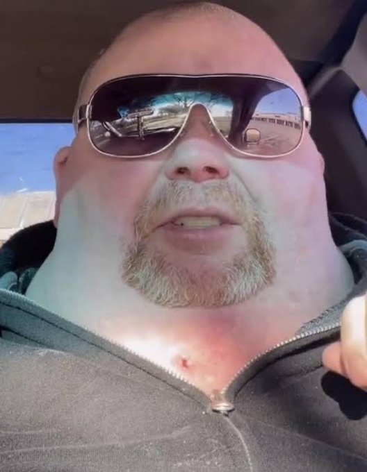 A close-up selfie of a heavily bearded, sunglasses-wearing man sitting in a vehicle, presented sarcastically as "the next doge." The glasses reflect an outdoor scene, emphasizing the casual, meme-like tone of the post mocking cryptocurrency hype.