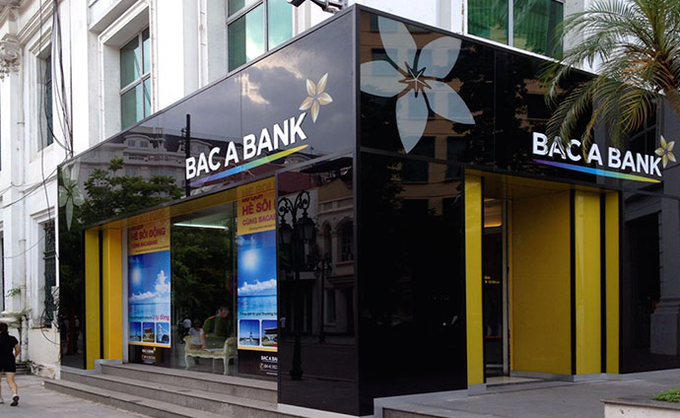 A street-level photograph of a "BAC A BANK" branch with a black and yellow storefront featuring a stylized flower logo.