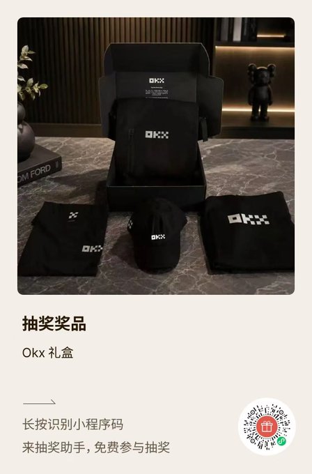 An elegant OKX VIP peripherals gift box display featuring a black t-shirt, hoodie, and cap arranged on a marble surface, with Chinese text "抽奖奖品" (Raffle Prize) and "Okx 礼盒" (Okx Gift Box) promoting the giveaway, alongside a mini-program QR code at the bottom for participation in the Qixi Festival-themed draw.