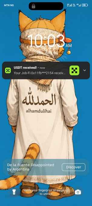 A smartphone lock screen at 10:03 AM on August 1 showing an animated cat in traditional Arab clothing with 'الحمدلله alhamdulillah' on its robe, featuring a USDT received notification from Job-Fi and a "De la Fuente Disappointed by Argentina" news alert.