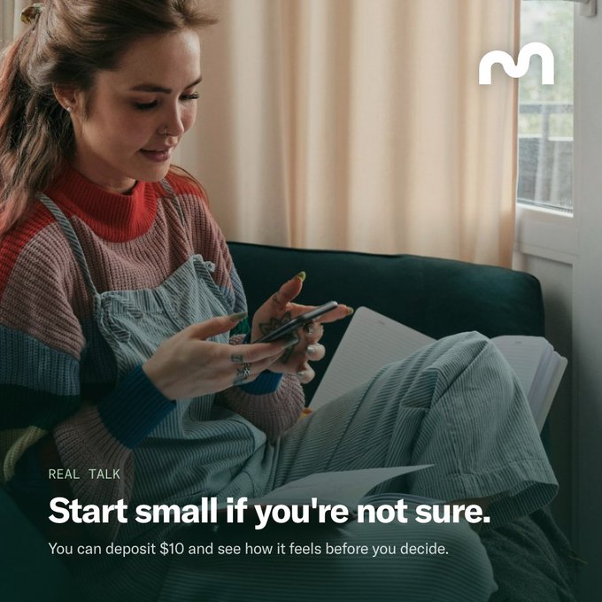 An advertisement featuring a young woman in a knit sweater sitting on a couch looking at her phone, with text reading 'REAL TALK: Start small if you're not sure. You can deposit $10 and see how it feels before you decide.' and an 'M' logo.