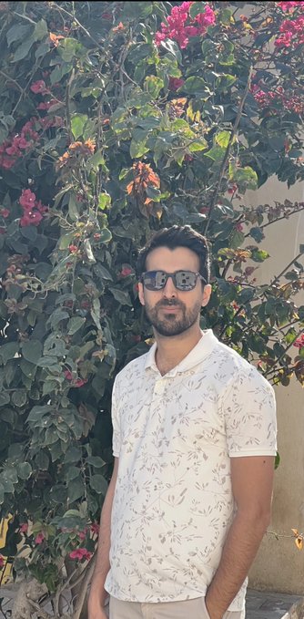 A man in sunglasses and a white patterned polo shirt stands in front of lush bougainvillea with vibrant pink blooms, embodying a fresh, sunny start to life after leaving his corporate career to pursue Web3 content creation. The bright outdoor setting reflects his bold pivot as a 39-year-old founder looking to connect with new brands.