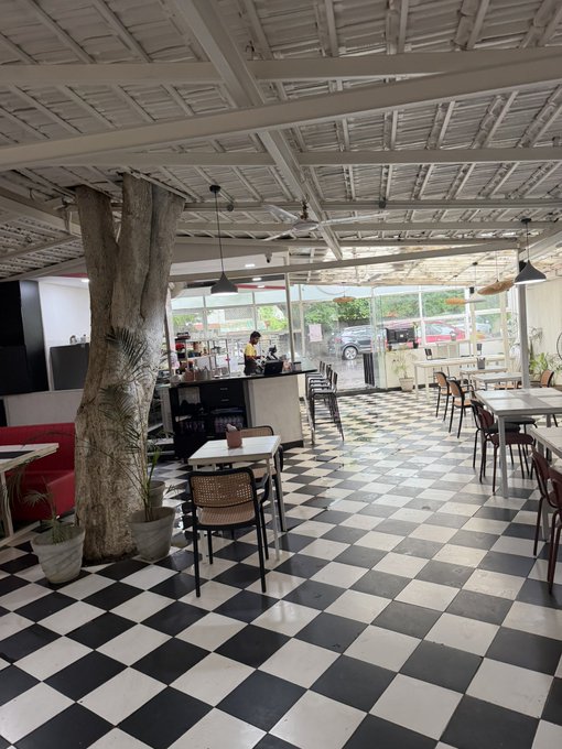 An open-air restaurant interior with a black and white checkered floor, a large tree growing through the ceiling, and a bar area in the background.
