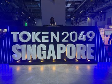 A DJ performs behind a large illuminated sign reading 'TOKEN2049 SINGAPORE' at the cryptocurrency conference.