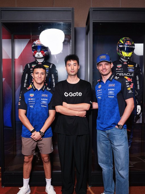 Gate's Head of KOC Godot戈多 poses for a photo with Oracle Red Bull Racing drivers Isack Hadjar and Max Verstappen at what appears to be a sponsorship event. The three stand in front of display cases showcasing racing helmets and suits bearing Oracle Red Bull Racing and Gate branding, highlighting Gate's partnership with the F1 team.