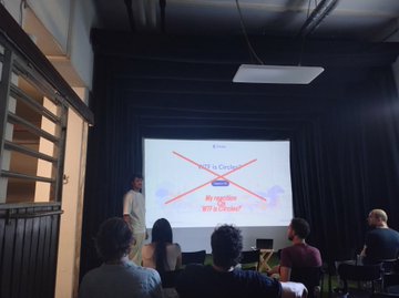 A presenter stands before an audience watching a slide at a meetup, with the screen displaying "Not a Congress, An Organizer, My Webdev Not a Unicorn" in crossed-out text. The image reflects the EthMunich community gathering, showing members engaging with content that humorously downplays grandiose titles in favor of hands-on, community-driven organizing.