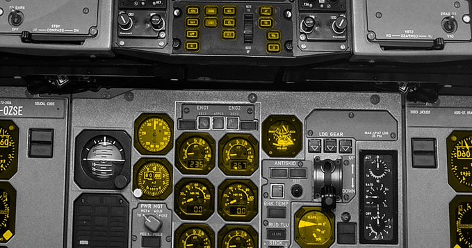Close-up of an aircraft cockpit instrument panel featuring illuminated yellow gauges, including altimeter (23,500), airspeed (335), and engine indicators (00.0), with controls for anti-skid, brake temp, and landing gear.