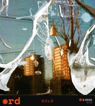 A photograph taken through a cracked or splattered window shows a city street scene with a building lit up in orange and a small bell hanging in the foreground, with text reading 'ord', 'SOLD', and '0.0035' at the bottom.